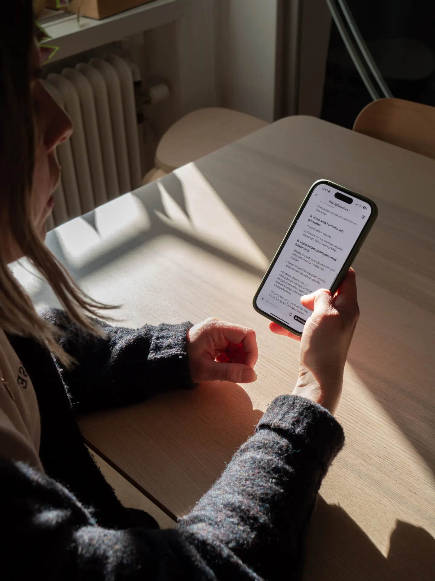 Person använder Generation Peps AI-hälsobot i mobilen vid ett köksbord